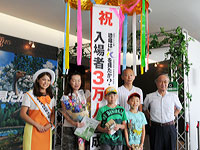 3万人目のご家族と、越前若狭観光宣伝隊の高橋亜由美さん、館長との記念写真